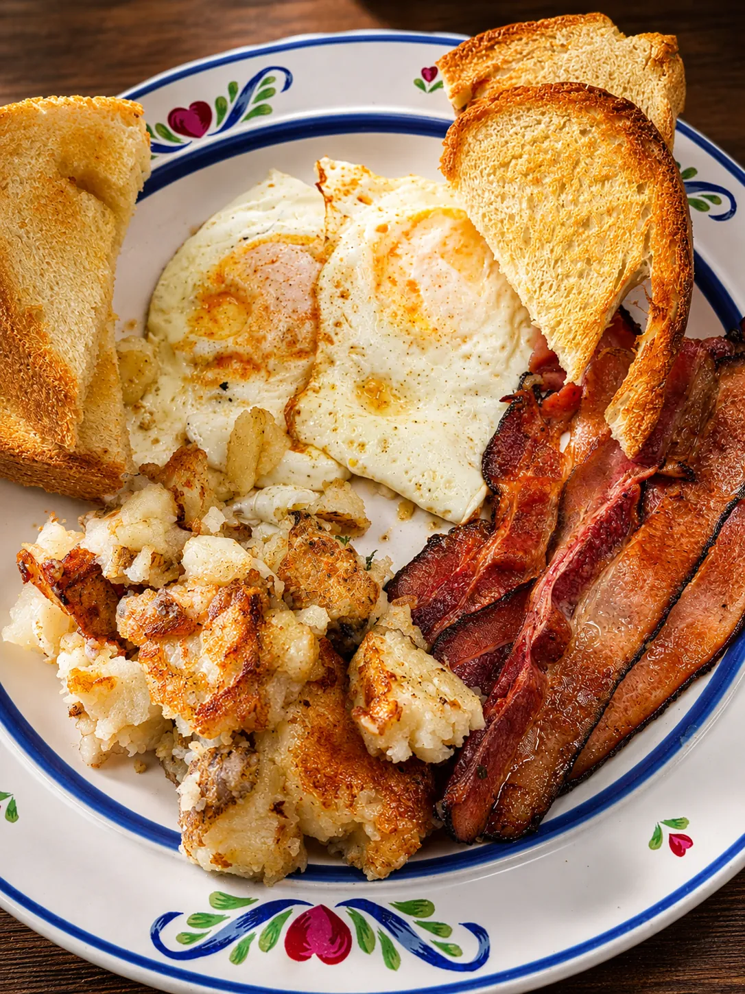 A breakfast plate with bacon, eggs, potatoes and toast